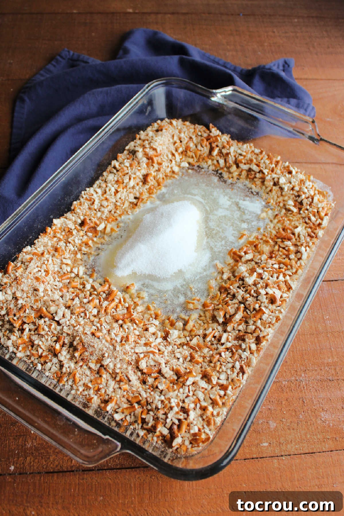 Melted butter, sugar, and crushed pretzels in 9x13-inch pan ready to be made into a crust.