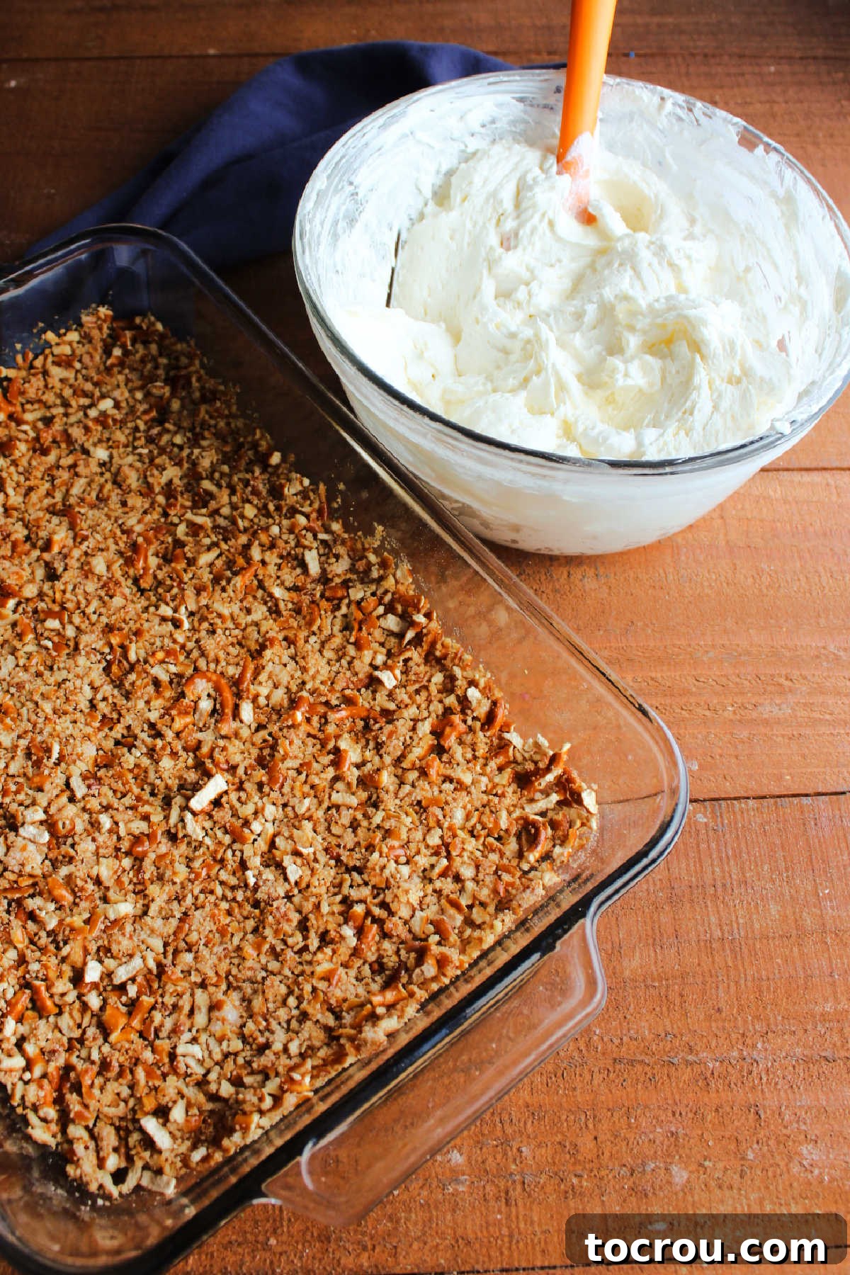 Pan with baked pretzel crust next to mixing bowl with fluffy cream cheese mixture ready to be layered.