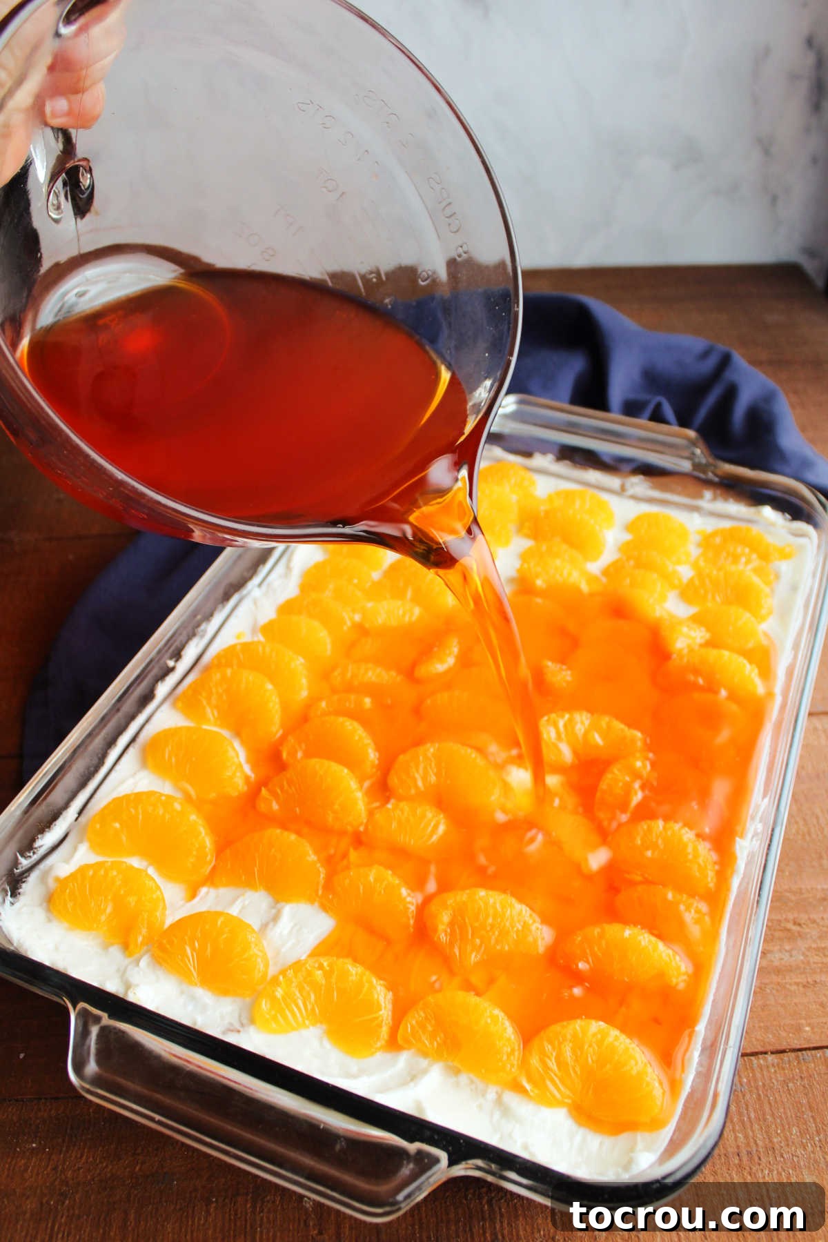 Pouring cooled orange Jello mixture over mandarin orange slices and cream cheese mixture.