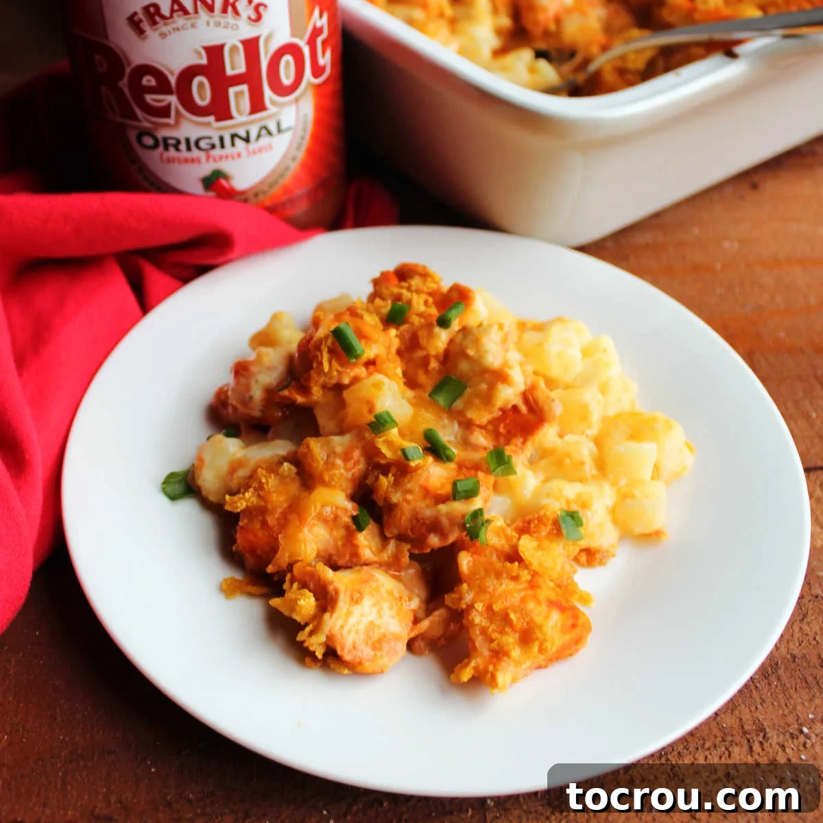A plate of golden, bubbling cheesy ranch potatoes crowned with spicy buffalo chicken and a crunchy cornflake topping, ready to be enjoyed.