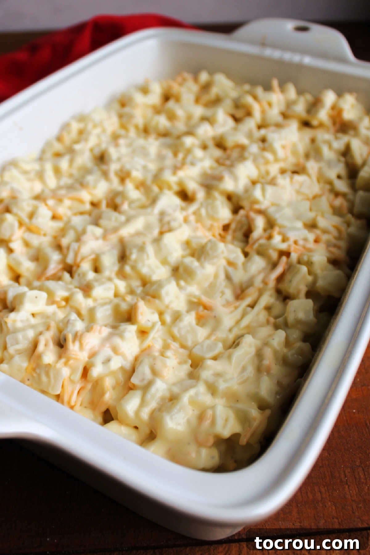Diced potatoes mixed with creamy ranch dressing, melted cheese, and condensed chicken soup, forming the rich base of the casserole in a baking dish.
