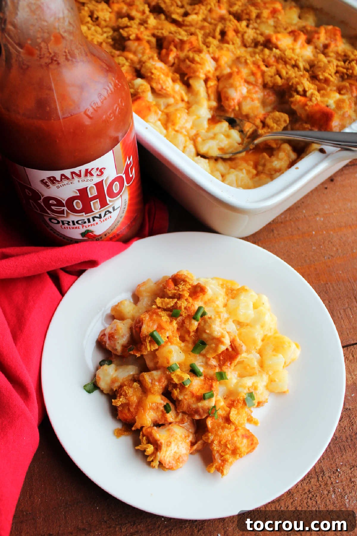 A dish of Ranch Potato and Buffalo Chicken Bake, with a bottle of Frank's Red Hot sauce in the background, hinting at the spicy flavors.