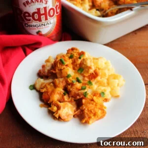 A plate of golden, bubbling cheesy ranch potatoes crowned with spicy buffalo chicken and a crunchy cornflake topping, ready to be enjoyed.