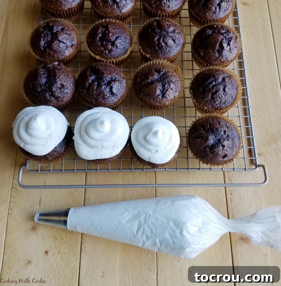 Toasted Marshmallow S'mores Cupcakes 7 Piping bag with toasted marshmallow buttercream next to chocolate cupcakes on cooling rack, getting ready to pipe swirls of frosting on top.