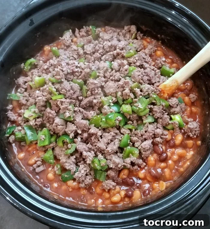Smoky Slow Cooker Chuckwagon Beans 4 ground beef and diced green peppers on top of beans in slow cooker.