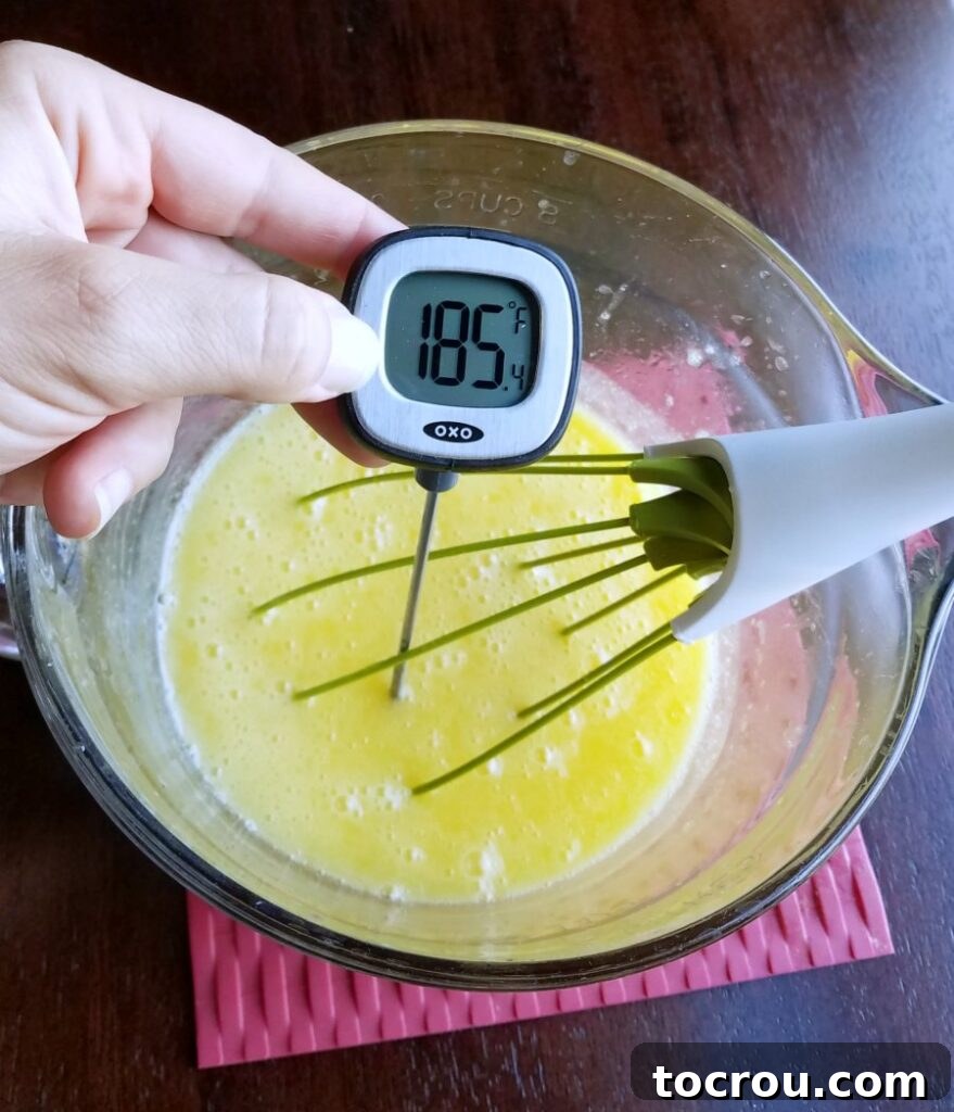 Checking Lemon Curd Temperature Hand holding an instant-read thermometer, showing a temperature of 185°F in a bowl of thickening lemon curd.