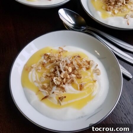 Bowl of yogurt topped with a swirl of homemade lemon curd and granola next to spoons, ready to eat.