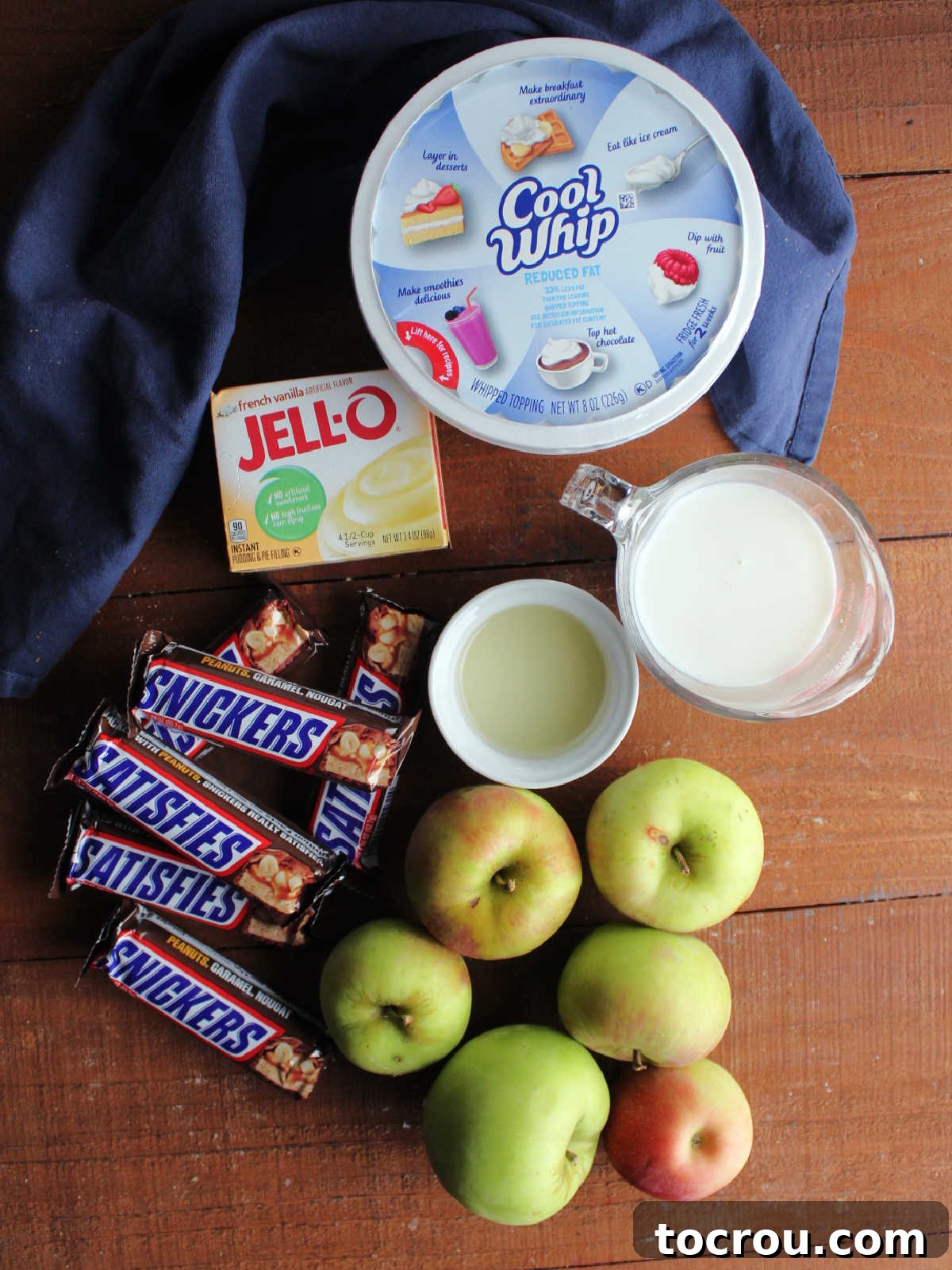 Decadent Apple Snickers Dessert 3 Ingredients including apples, snickers candy bars, pudding mix, milk, lemon juice, and cool whip ready to be made into a candy bar salad.