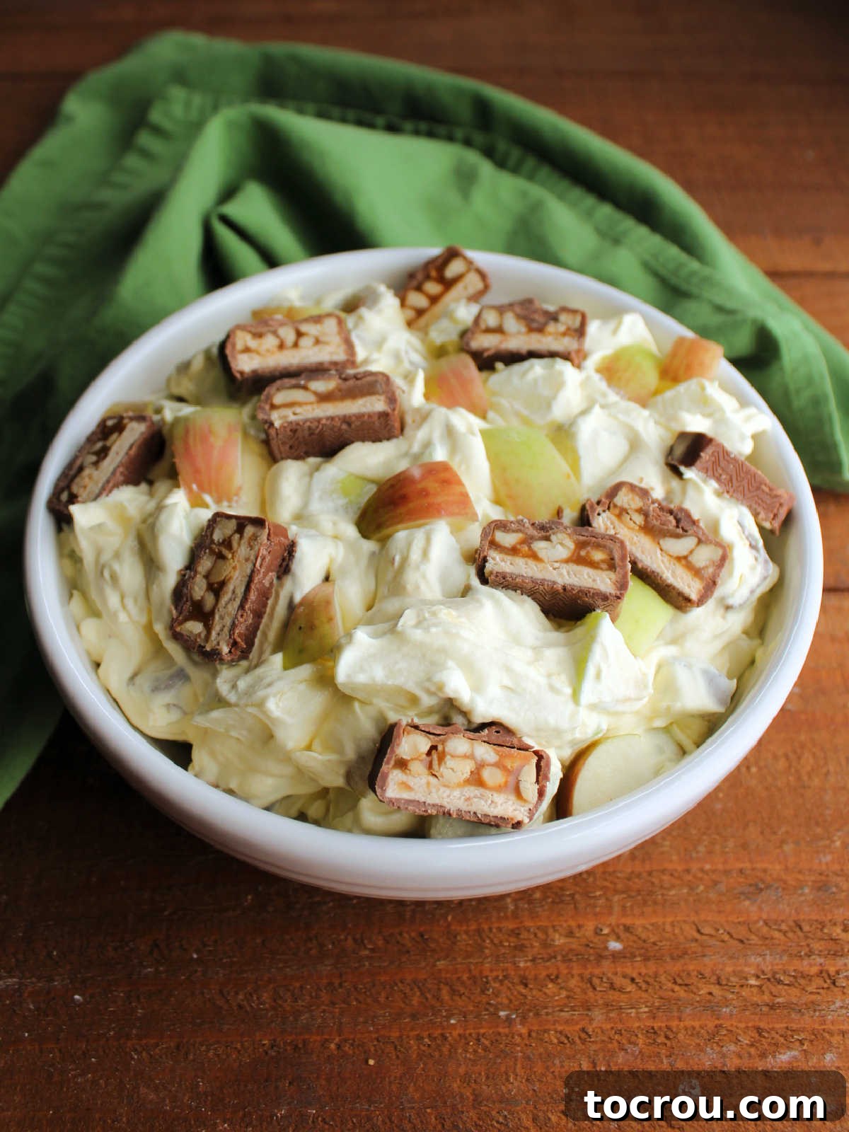 Decadent Apple Snickers Dessert 6 Serving bowl filled with chilled creamy snickers salad garnished with extra chunks of candy bar and fresh apples.
