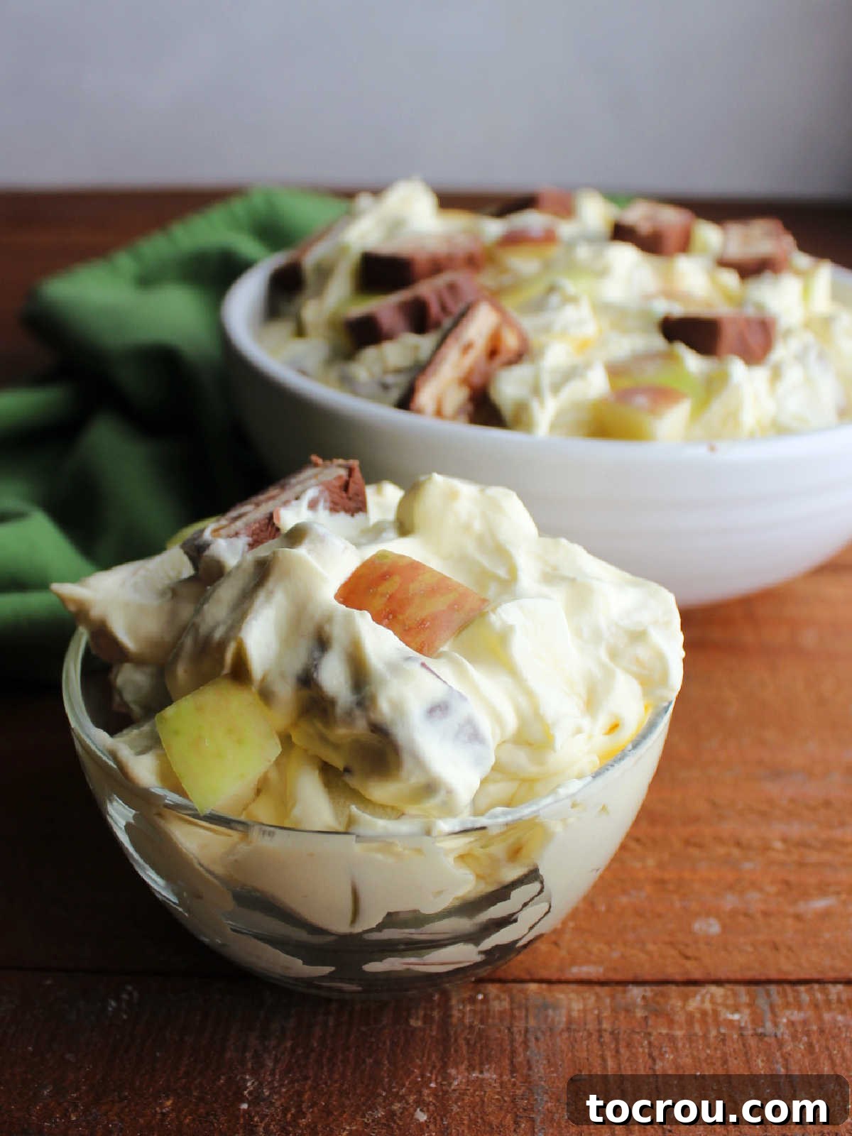 Decadent Apple Snickers Dessert 7 Small glass bowl of snickers apple salad in front of a serving bowl with more fluff salad in the background.