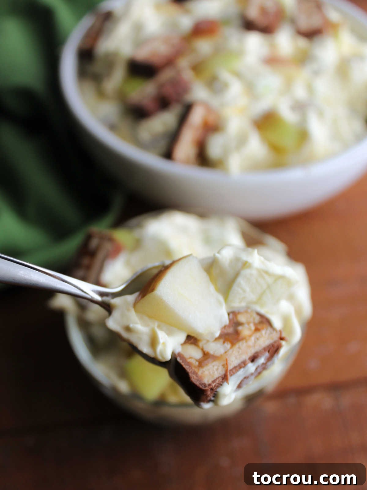 Decadent Apple Snickers Dessert 8 Bite of apple snickers salad on spoon showing chunk of candy bar, fresh apples, and creamy vanilla pudding dressing.