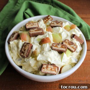 Serving bowl filled with creamy apple snickers salad topped with extra chunks of fresh apple and bits of Snickers candy bars.