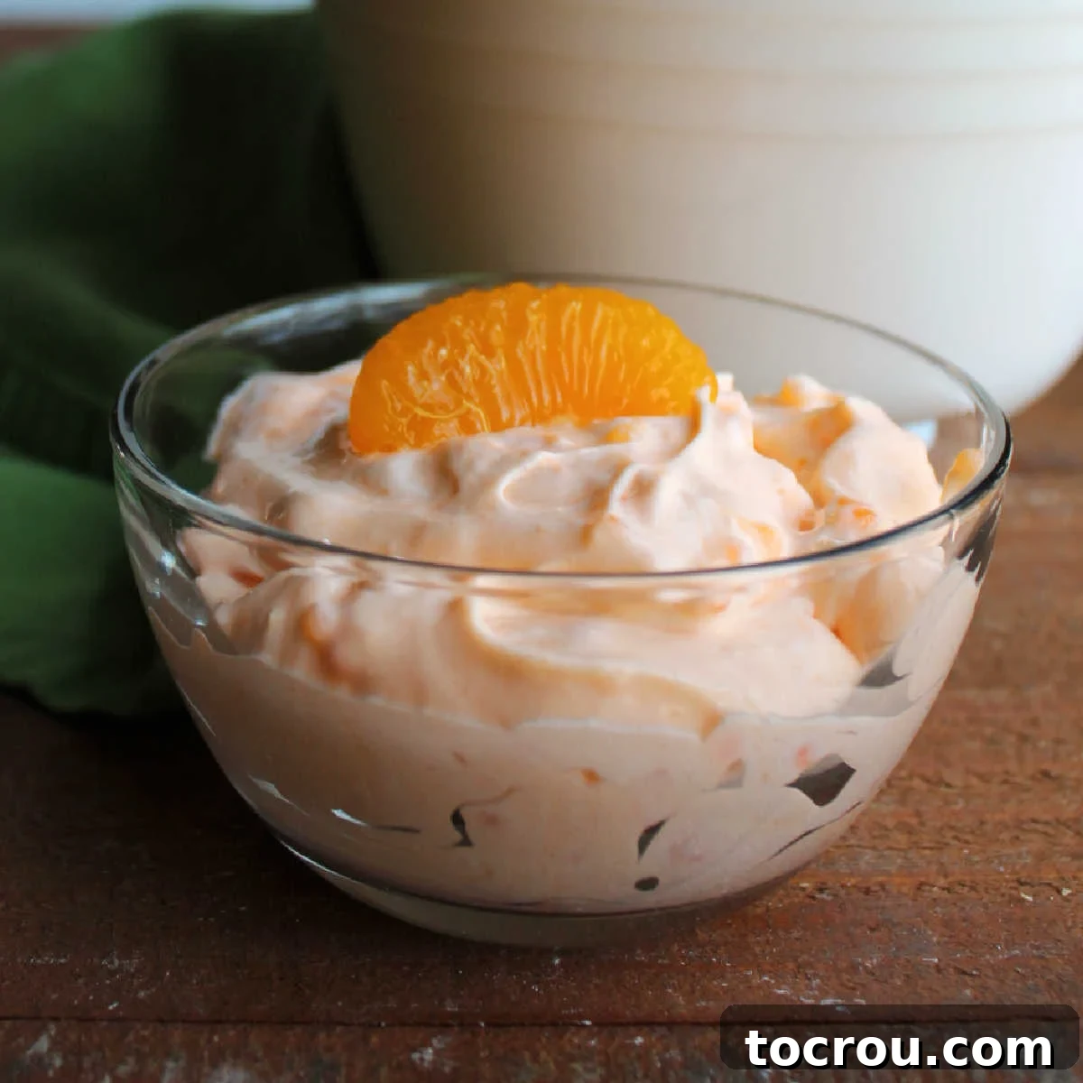 small glass bowl filled with orange fluff salad with bits of tapioca inside topped with a mandarin orange slice.