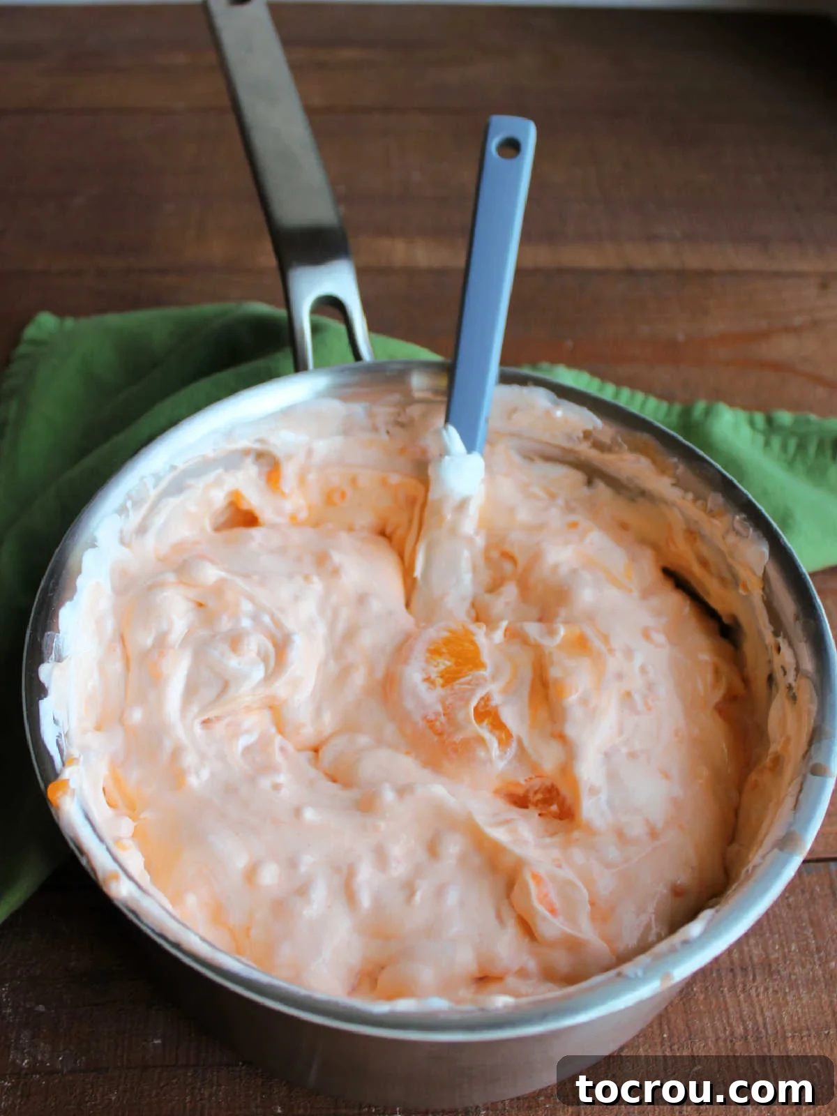 Saucepan filled with orange fluff mixture showing creamy and airy texture with pale orange color and bits of tapioca and oranges inside. 