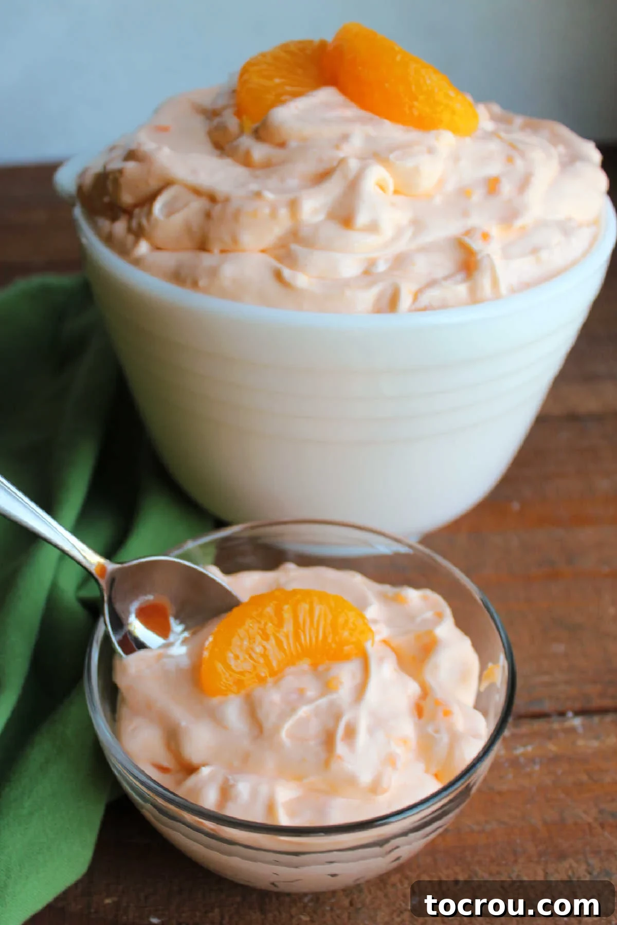 Spoon dipping into a small bowl of orange fluff salad with tapioca and cool whip. 