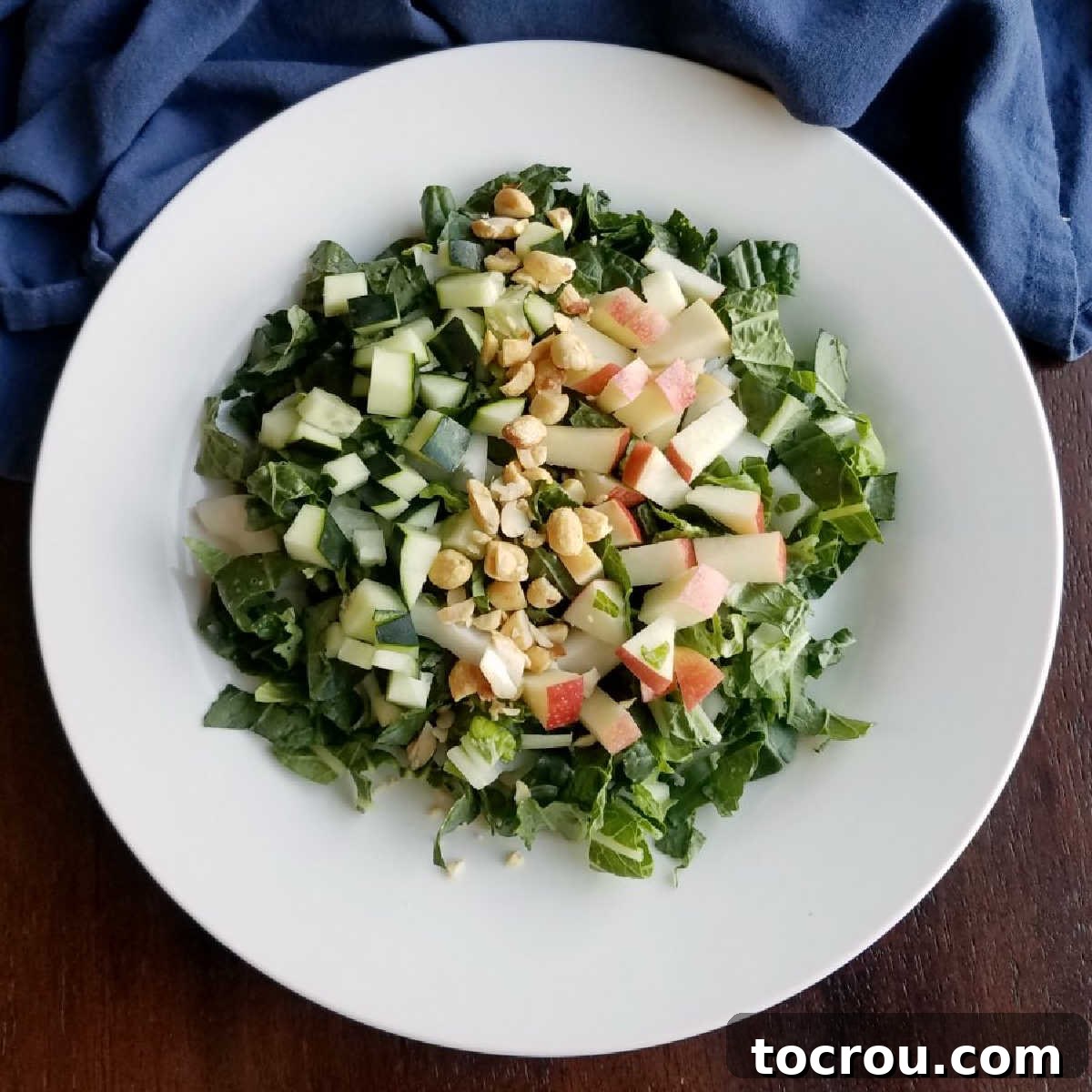 A delightful bowl of Bok Choy Salad, showcasing crisp bok choy, vibrant apple slices, crunchy peanuts, and a creamy homemade peanut yogurt dressing artfully drizzled over the top.