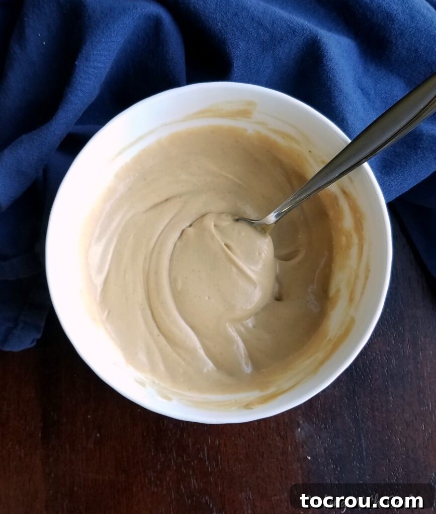 A close-up shot of a bowl filled with a creamy, rich peanut yogurt salad dressing, showcasing its smooth texture and appetizing color.