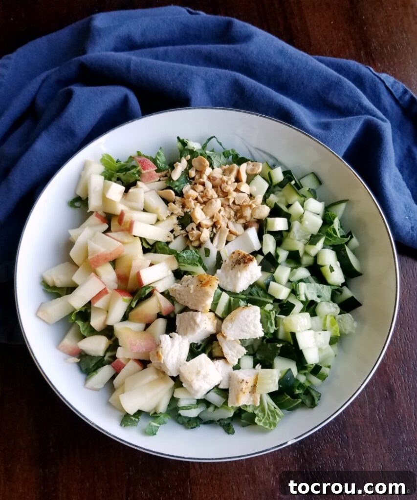 A generously sized bowl filled with freshly chopped bok choy, garnished with diced apples, crisp cucumbers, and tender pieces of cooked chicken, making it a complete meal.