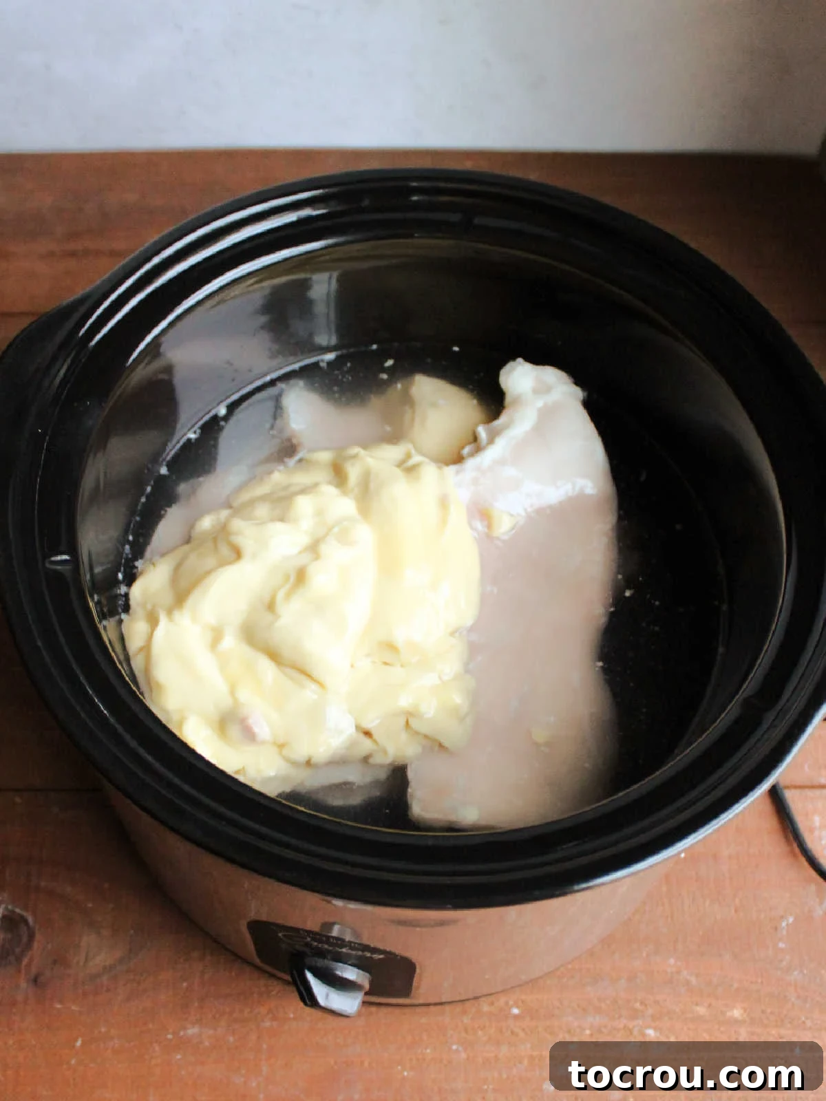 Crockpot with chicken breasts, chicken broth, and cream of chicken soup inside, ready to be cooked. 