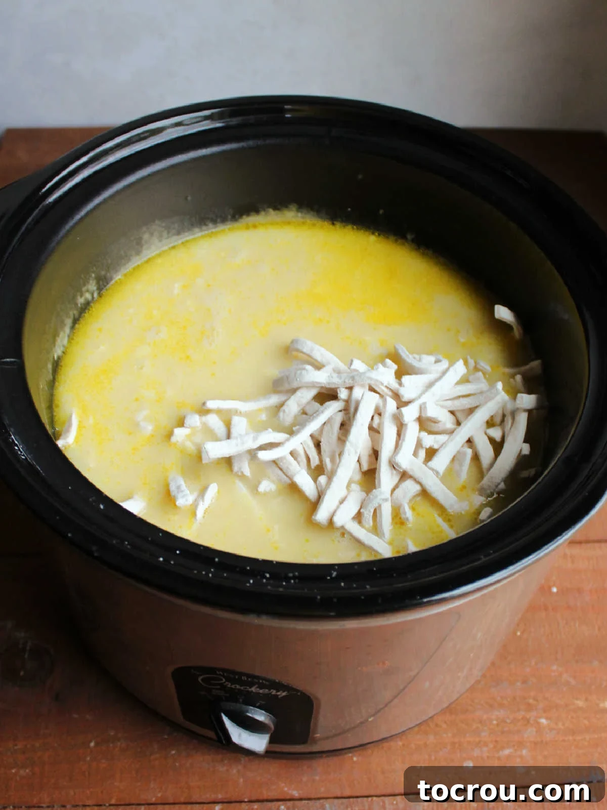 Crockpot after the chicken has been cooked and shredded and frozen egg noodles have been added, ready to finish cooking. 