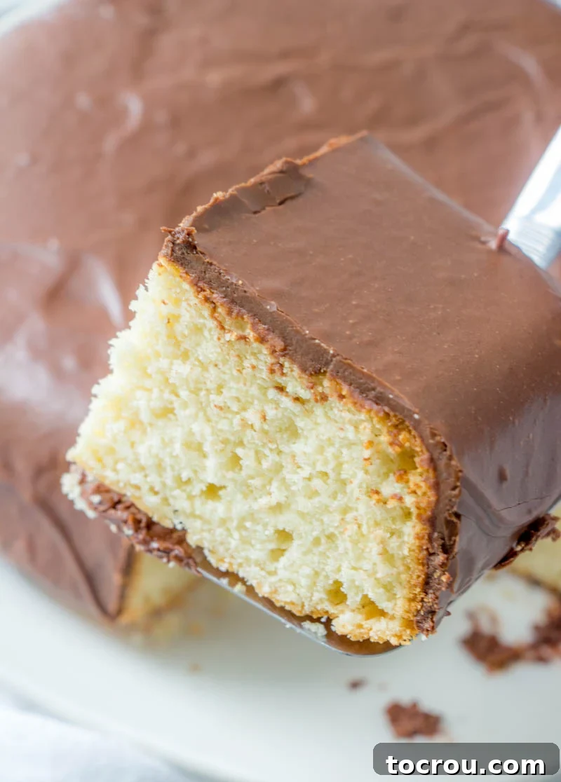 A perfect slice ready to be savored Lifting a square piece of vanilla Farmer's Daughter Cake with a generous layer of fudge frosting from a cake plate.