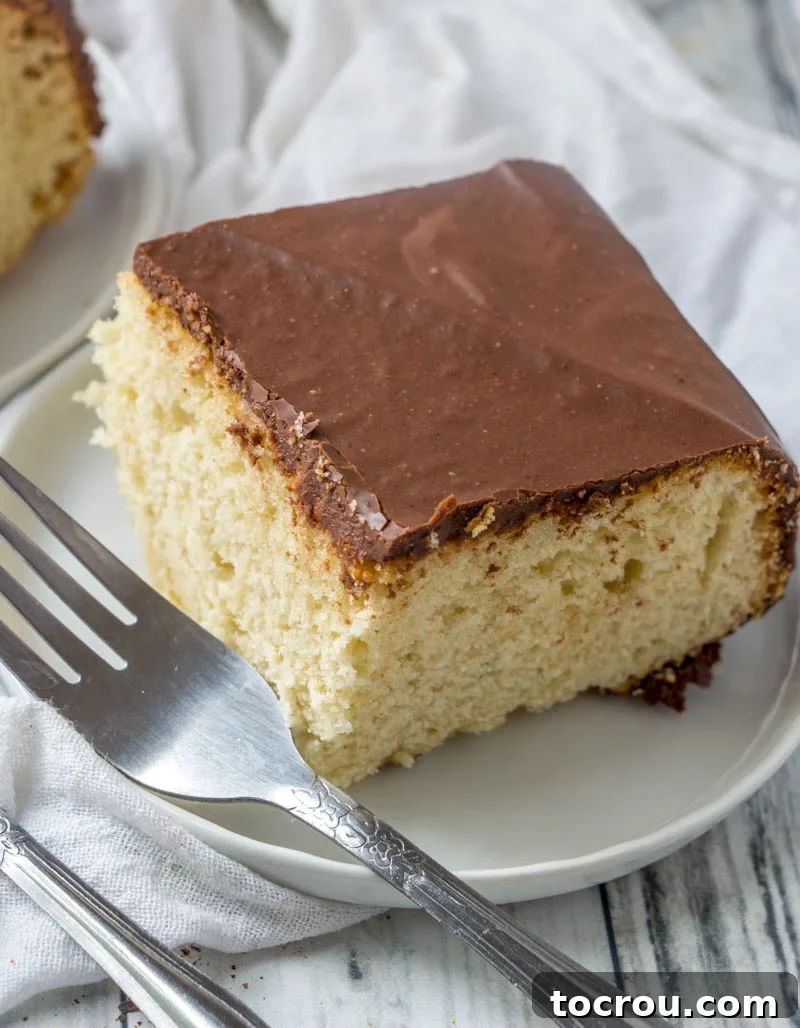 Irresistible Slice of Cake with Fudge Frosting Piece of creamy vanilla cake topped with fudgy icing on a plate with a fork, ready to be enjoyed.