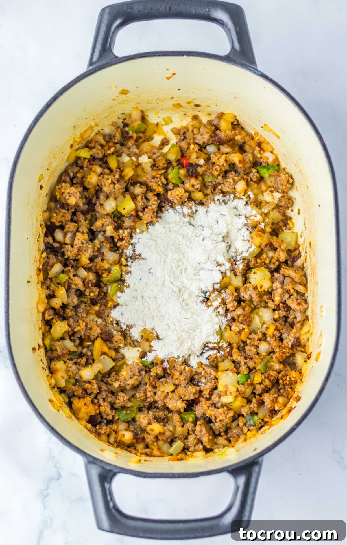 Adding Flour for Roux Flour being added to the browned sausage and cooked vegetable mixture in a Dutch oven, forming the roux for a thick, creamy soup.