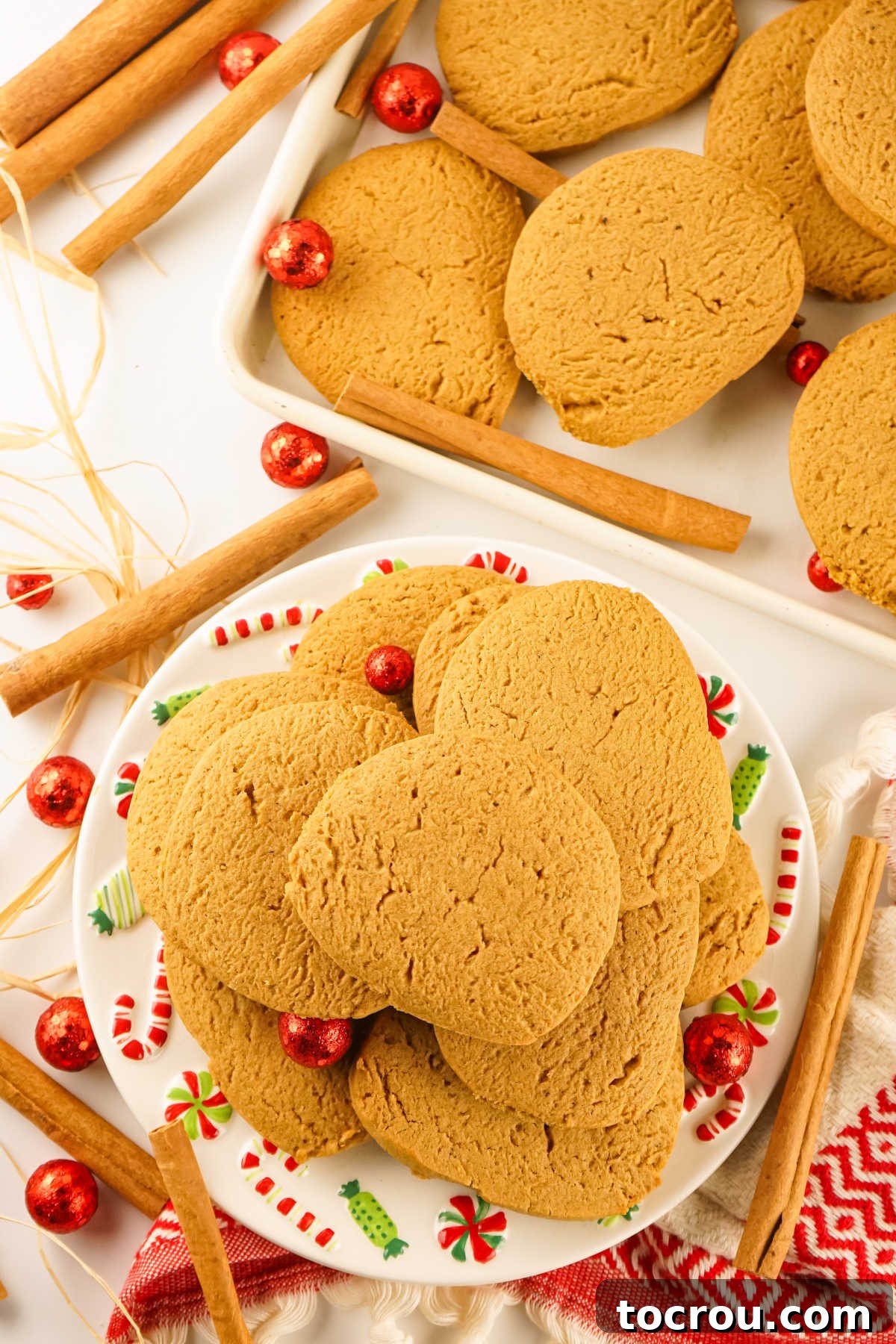 Plate of freshly baked gingersnap cookies with remaining cookies on baking tray nearby.