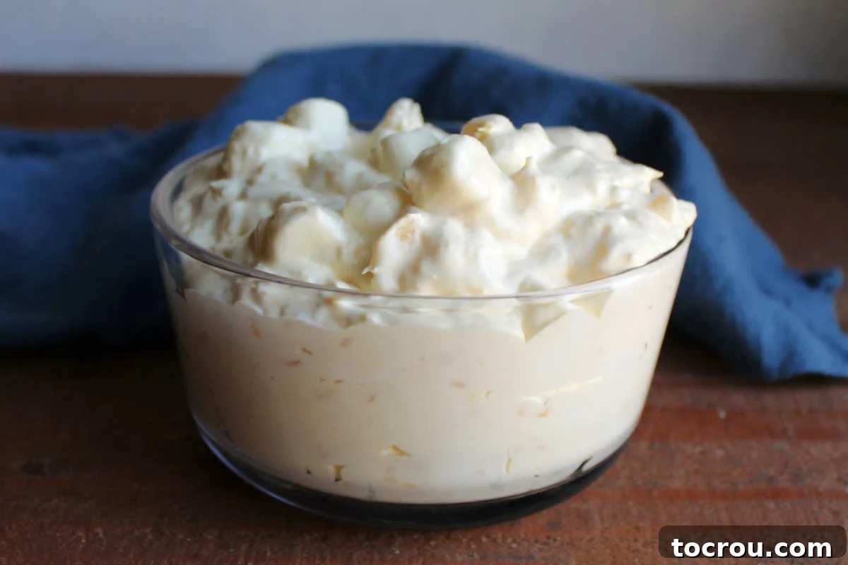 Glass bowl filled with creamy pineapple fluff, adorned with mini marshmallows and a luscious pudding and whipped topping base. 