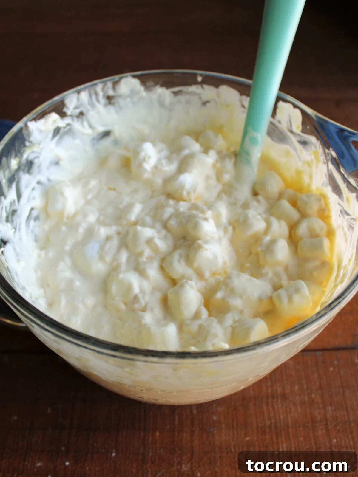 A mixing bowl filled with pineapple fluff salad, featuring visible mini marshmallows, crushed pineapple, and the creamy vanilla pudding and whipped topping mixture, ready for chilling.