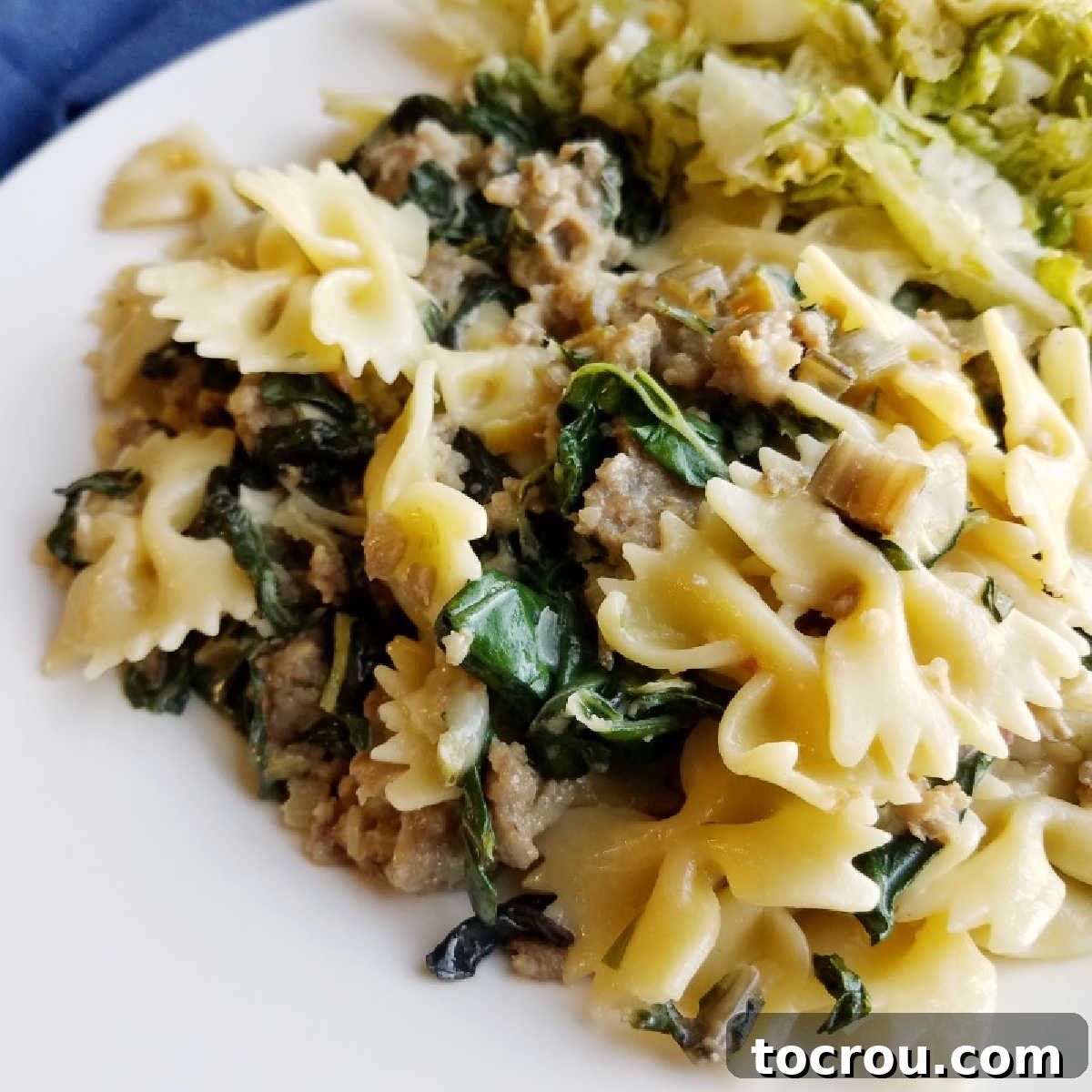 Close-up of a serving of creamy pasta with wilted greens and Italian sausage, garnished with fresh herbs and Parmesan.