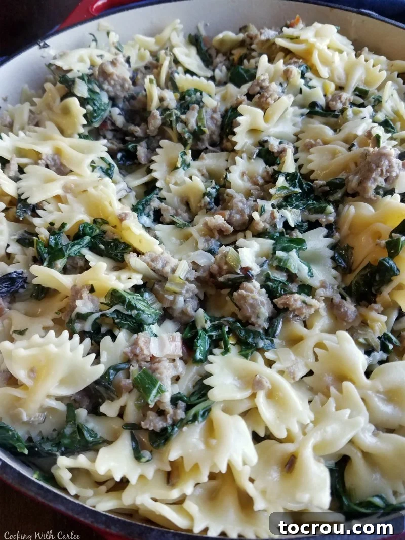 A pot of creamy bowtie pasta mixed with wilted greens and savory Italian sausage, ready to be served.