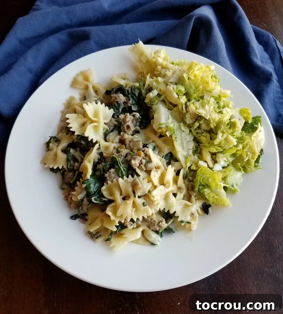 A serving of creamy pasta with sausage and chard on a plate, accompanied by a fresh side salad.