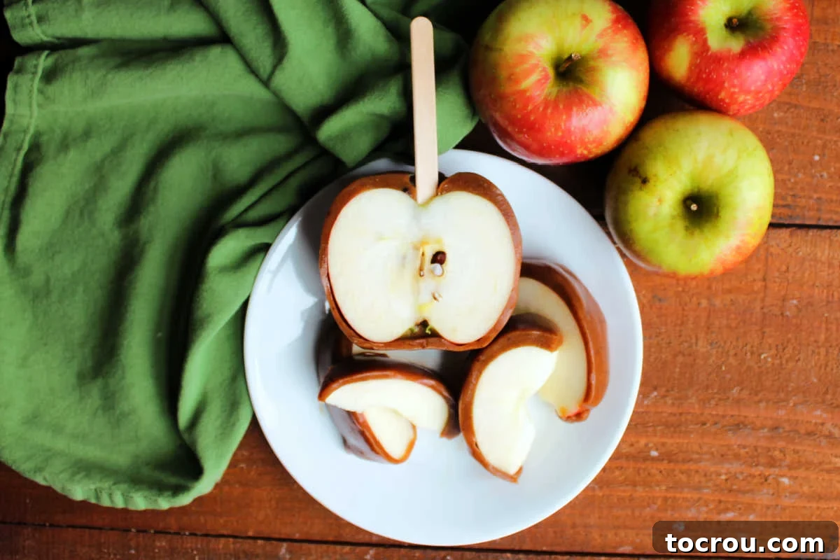 Plate with half of a caramel apple made using homemade caramel wraps next to sliced apples with thick layer of homemade caramel on the outsides, ready to enjoy. 