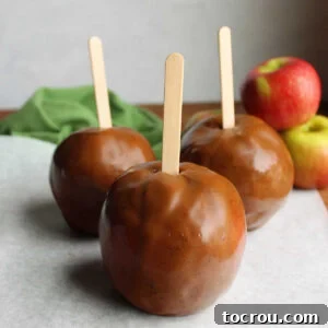 Three caramel apples made using homemade caramel apple wraps on sticks, ready to be served.