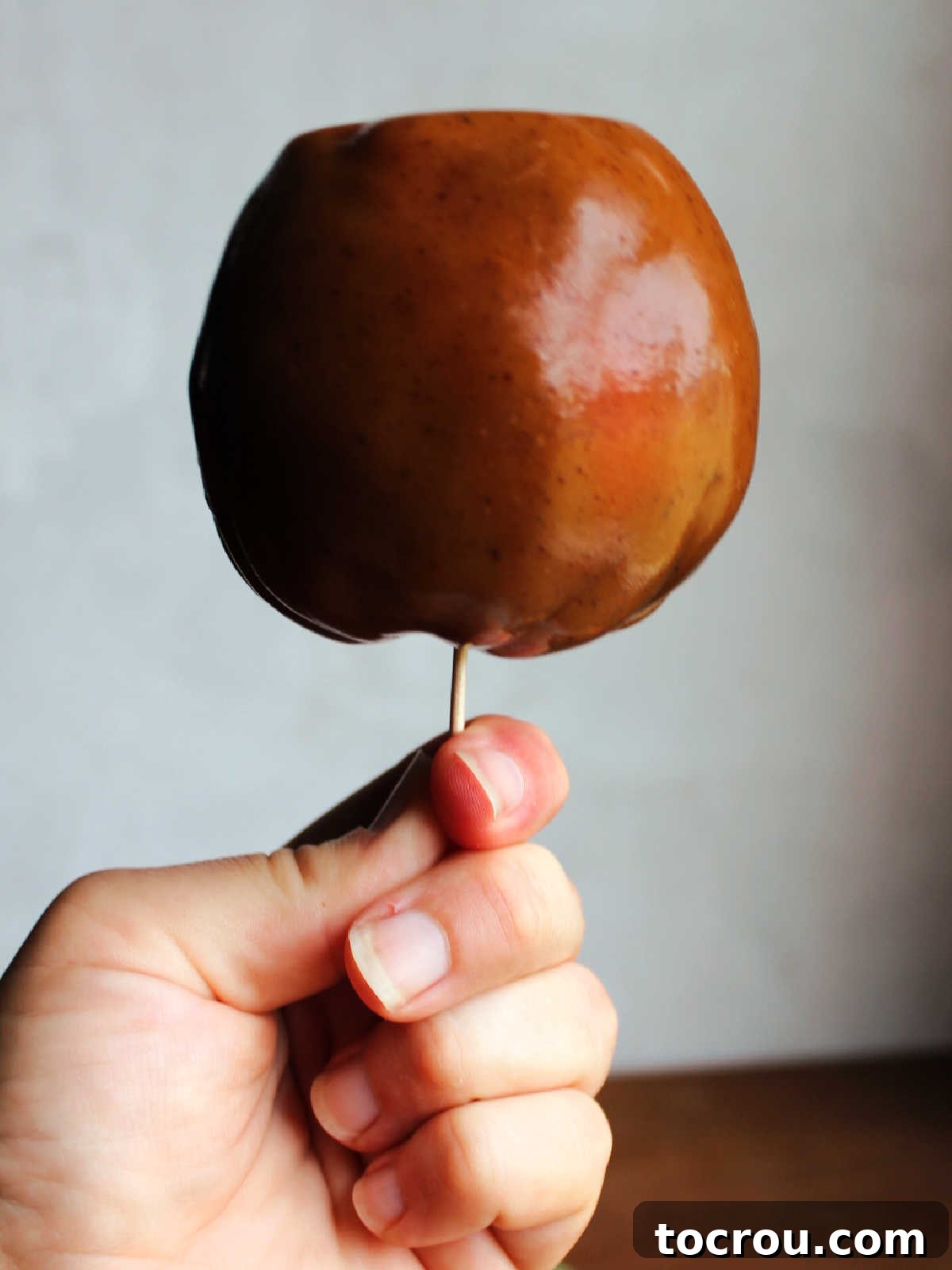 Hand holding caramel apple on a stick, showing the caramel after it has been smoothed around the apple. 