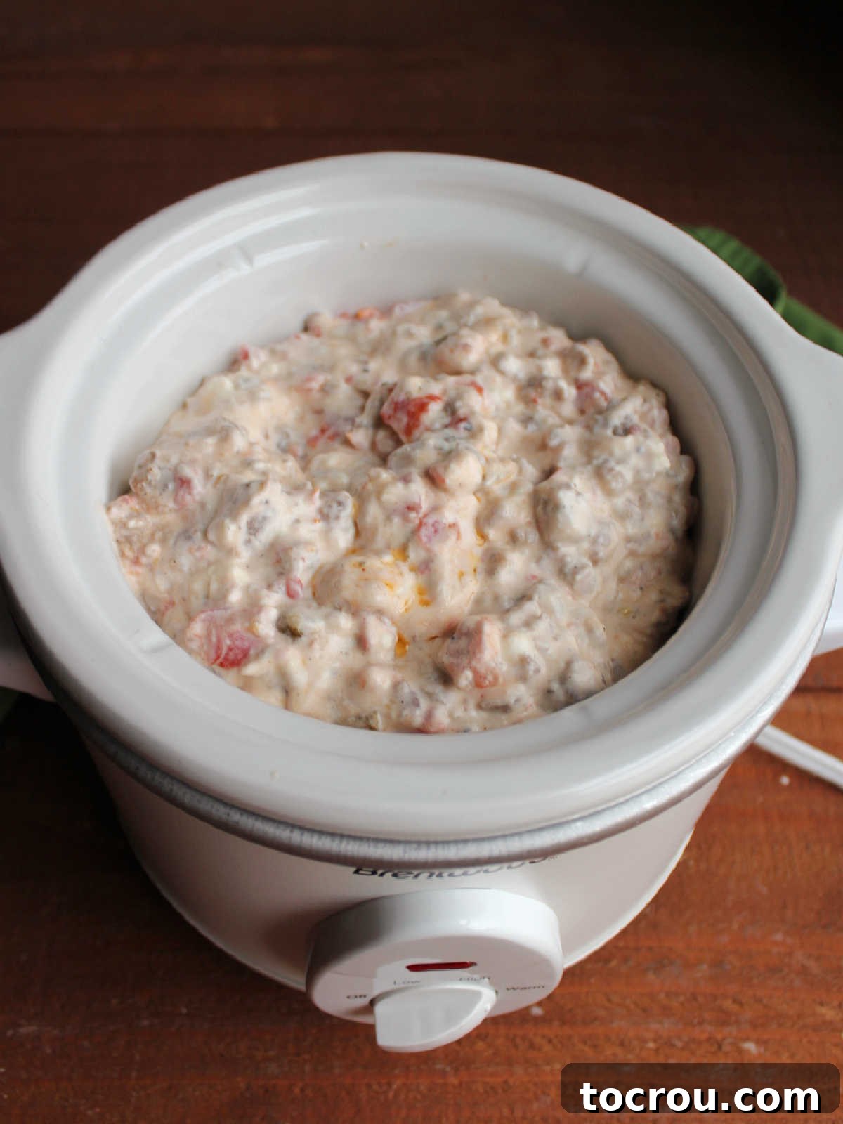 Small slow cooker with cream cheese and sausage rotel dip inside to keep warm.