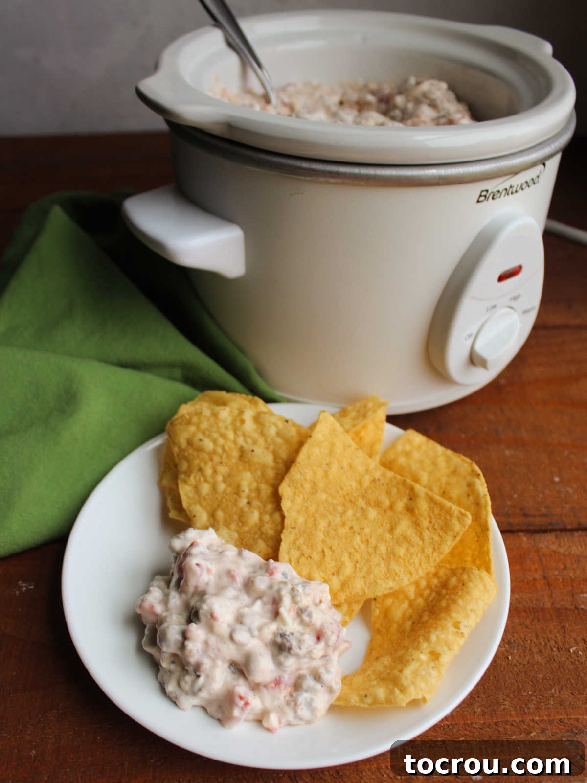 Plate of creamy sausage rotel dip and chips next to the crockpot with more dip staying warm inside.