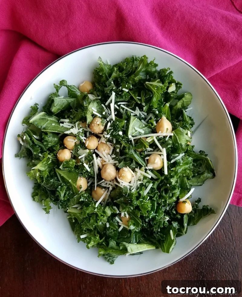 Lemony Kale and Chickpea Salad A vibrant bowl of simple kale salad featuring fresh kale, chickpeas, and a sprinkle of Parmesan cheese, garnished with lemon wedges.