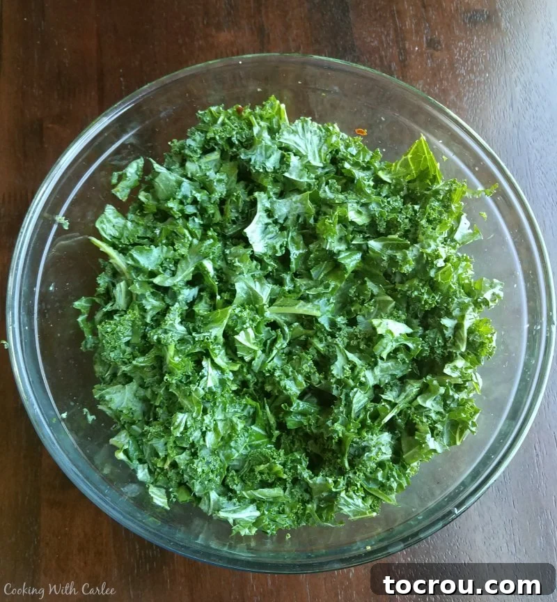 Massaged Kale with Dressing A close-up shot of a bowl filled with finely chopped kale, visibly coated in dressing, illustrating the process of massaging kale to soften its texture.