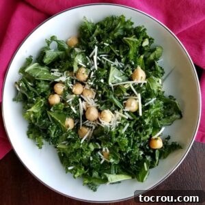 A vibrant bowl of simple kale salad featuring fresh kale, chickpeas, and a sprinkle of Parmesan cheese, garnished with lemon wedges.