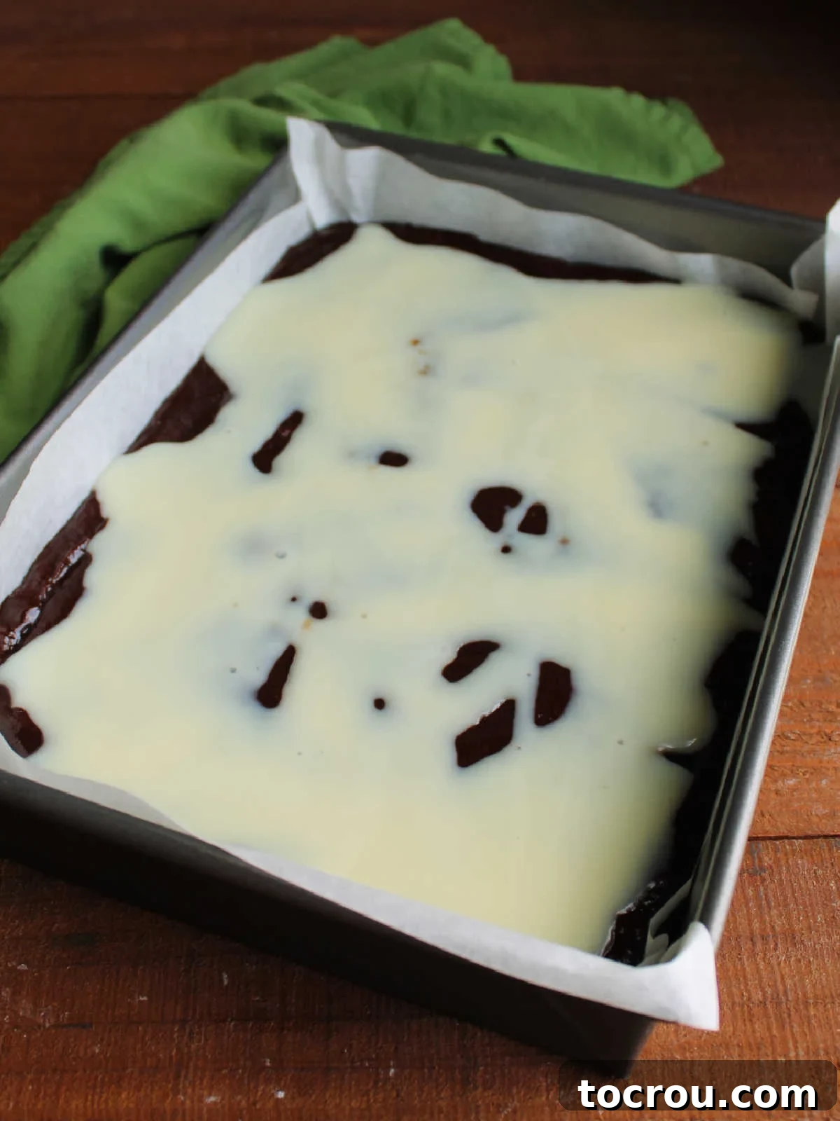 Can of sweetened condensed milk drizzled over brownie batter in a parchment paper lined 9x13-inch pan.