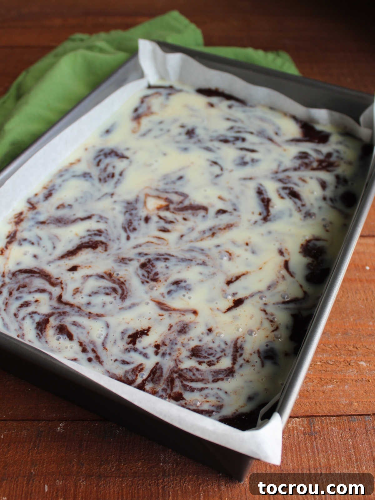 The pan after a knife was used to swirl the condensed milk into the brownie mix some, showing a fair amount of condensed milk on top still but more brownie batter showing through than before.