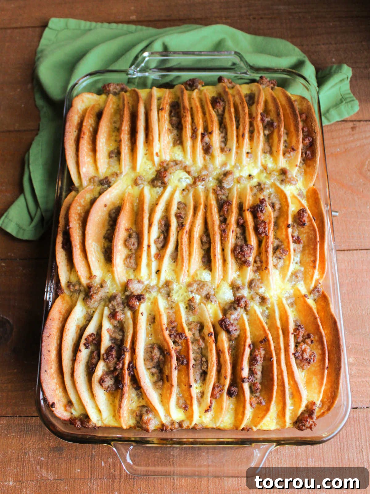 Baked casserole showing toasted edges on the pancakes with sausage between the layers and most of the egg mixture soaked into the pancakes giving them a french toast like texture. 