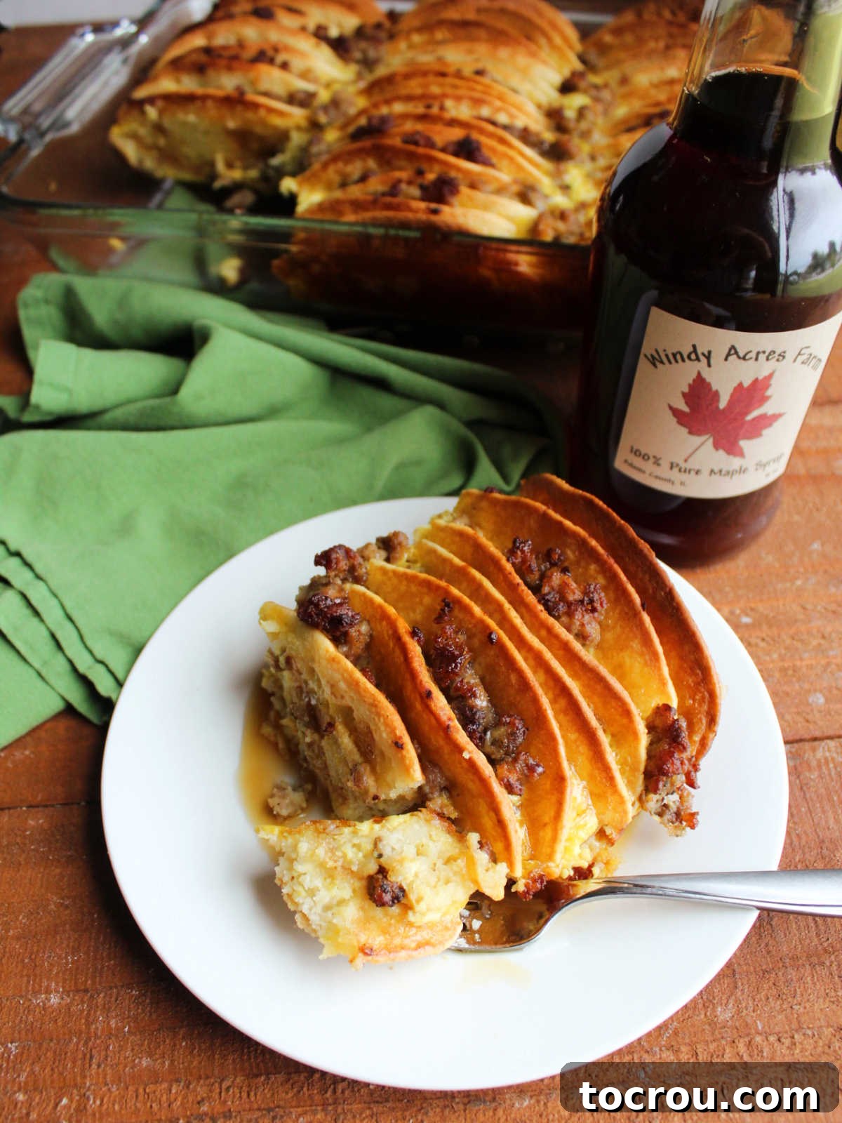 Bite of pancake and sausage bake on fork showing the fluffy texture of the pancakes after they have soaked in the egg mixture, ready to eat. 