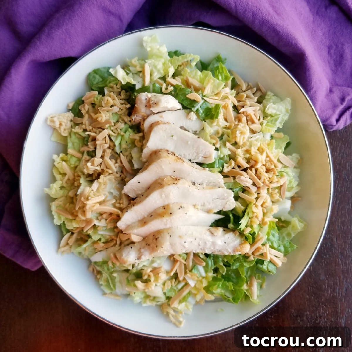 Bowl of napa salad with sweet and sour dressing, crunchy ramen and sunflower seeds and sliced chicken on top.