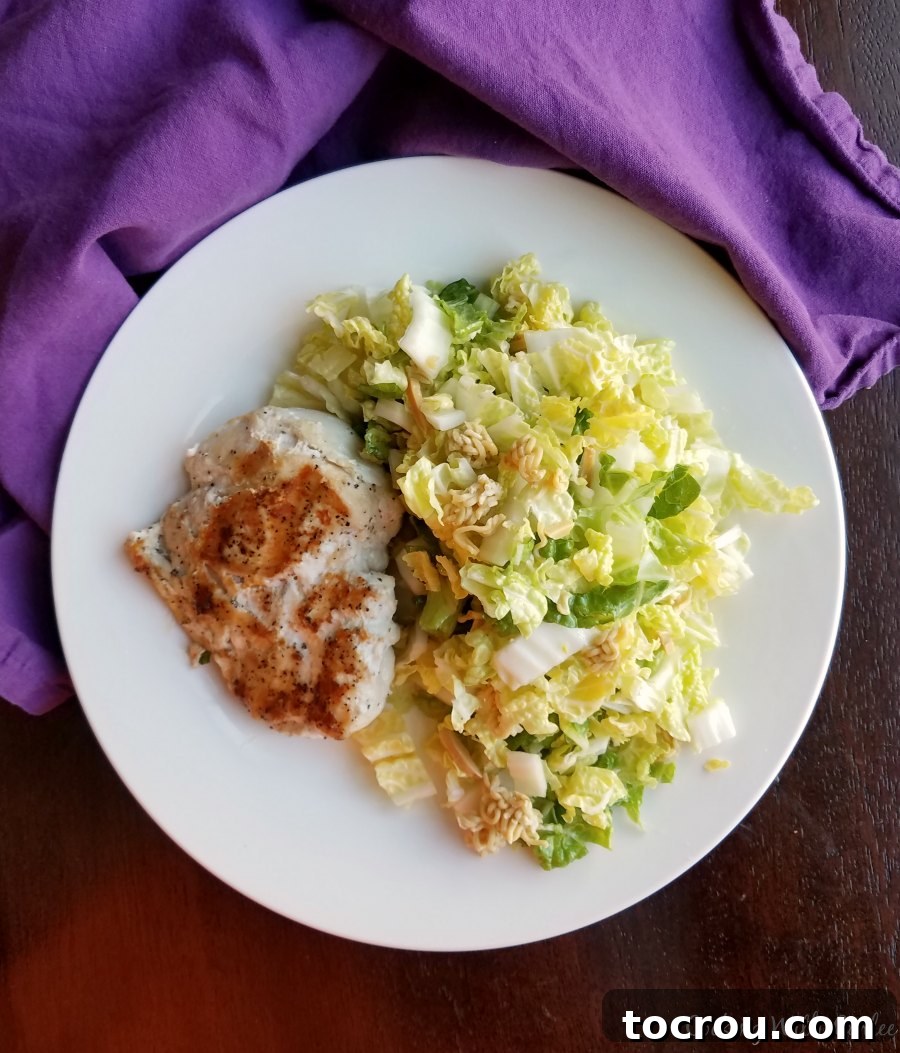 dinner plate with napa salad on one side and a chicken breast on the other.