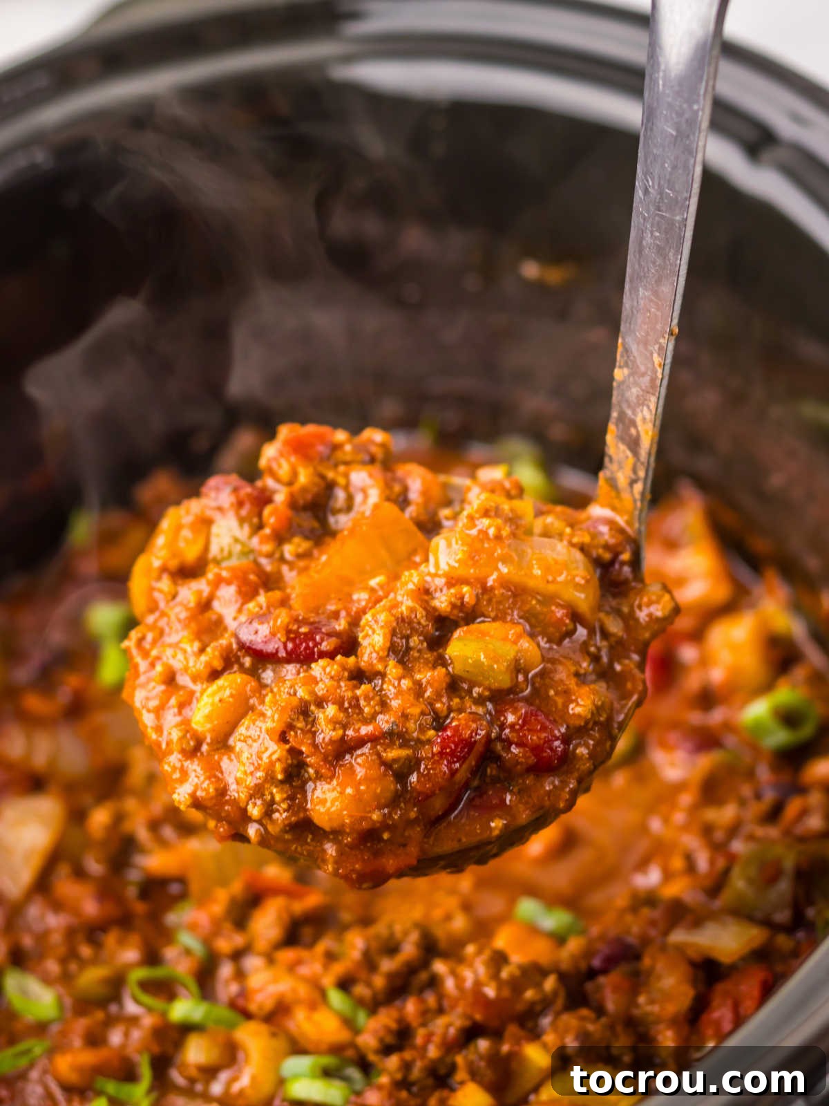 Ladle scooping thick, spiced Wendy's chili from a slow cooker, showing the rich blend of beans, vegetables, and ground beef.