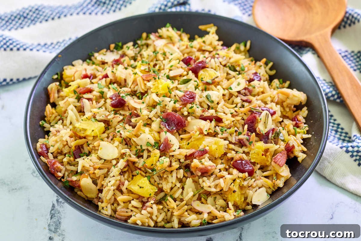 Orange Cranberry Rice Pilaf Large bowl of vibrant Orange Cranberry Rice Pilaf, garnished with fresh orange segments, whole cranberries, chopped herbs, and slivered almonds, ready to be served.