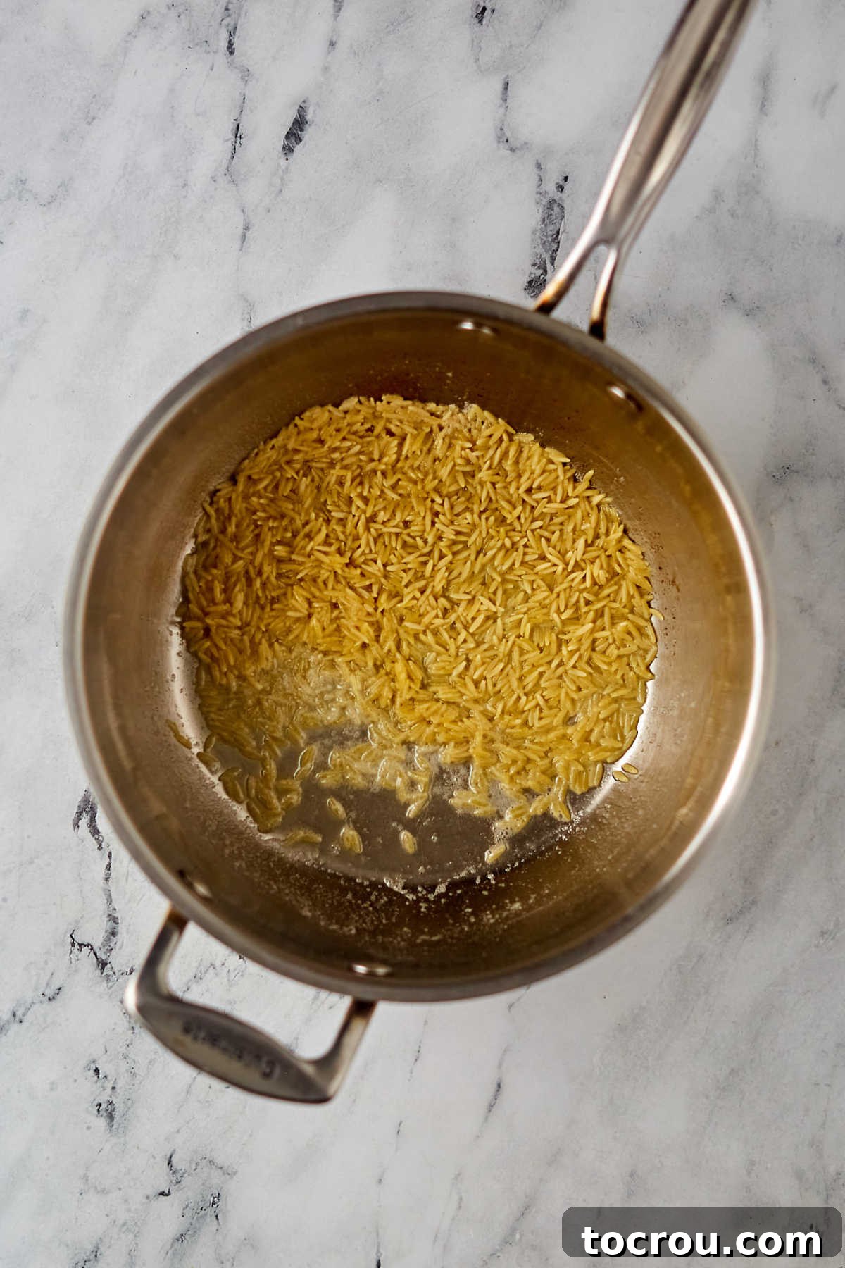 Toasting Orzo in Butter Close-up view of orzo pasta being toasted in melted butter in a saucepan, turning golden brown as it cooks for the rice pilaf.